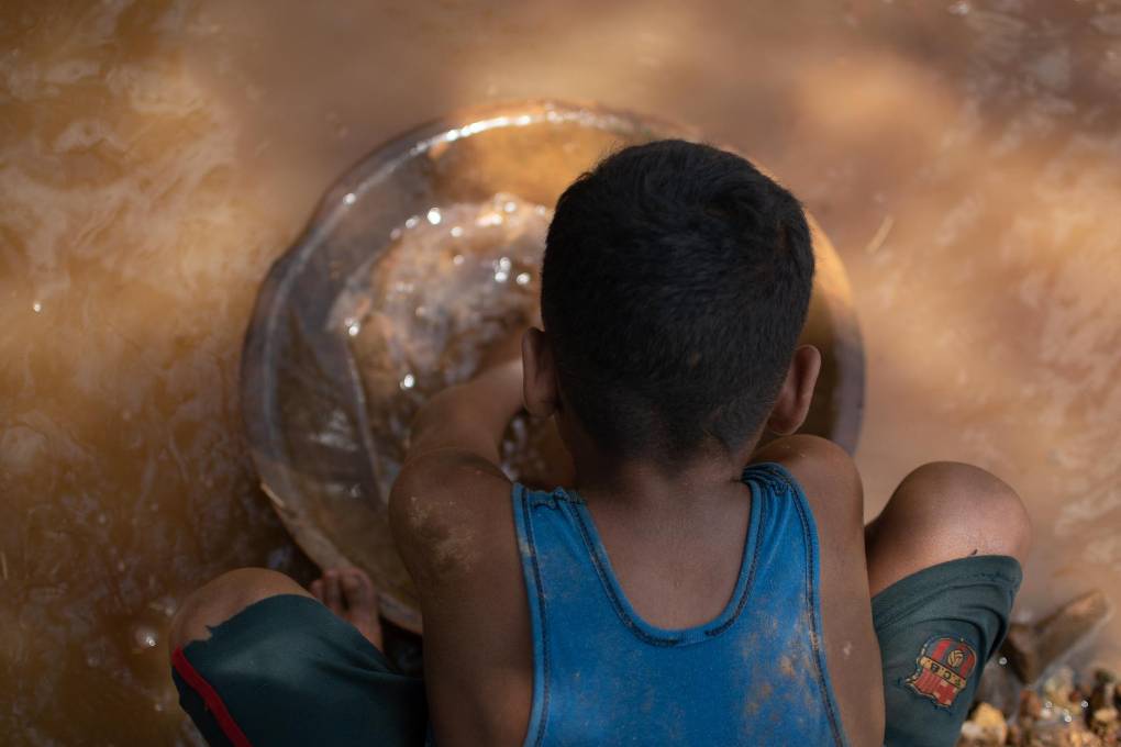 Un niño minero venezolano descarga una bolsa de barro en un recipiente.