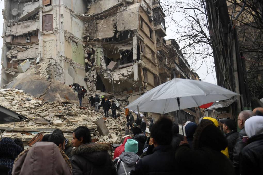 Los espectadores observan cómo los equipos de rescate buscan sobrevivientes bajo los escombros de un edificio derrumbado después de un terremoto en la ciudad de Alepo, en el norte de Siria, controlada por el régimen.