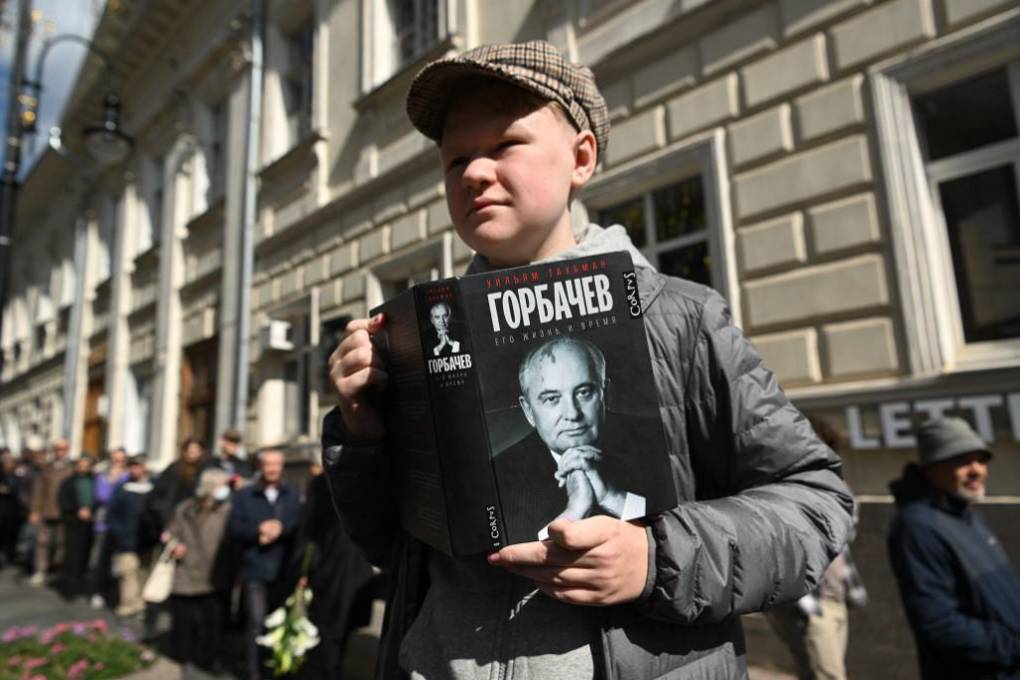 Un hombre sostiene un libro con el retrato de Mikhail Gorbachev mientras hace cola para asistir a una ceremonia de despedida.