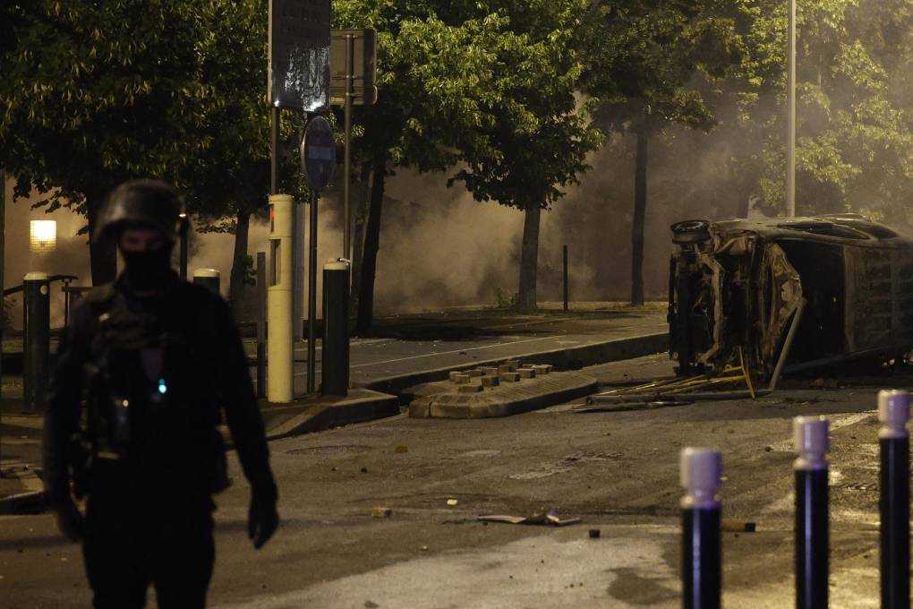 Un policía hace guardia junto a los restos de un automóvil quemado durante las protestas en Nanterre.