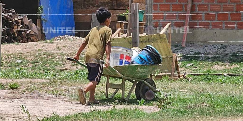 Un niño con carrtilla busca agua cargando botes sobre una carretilla.